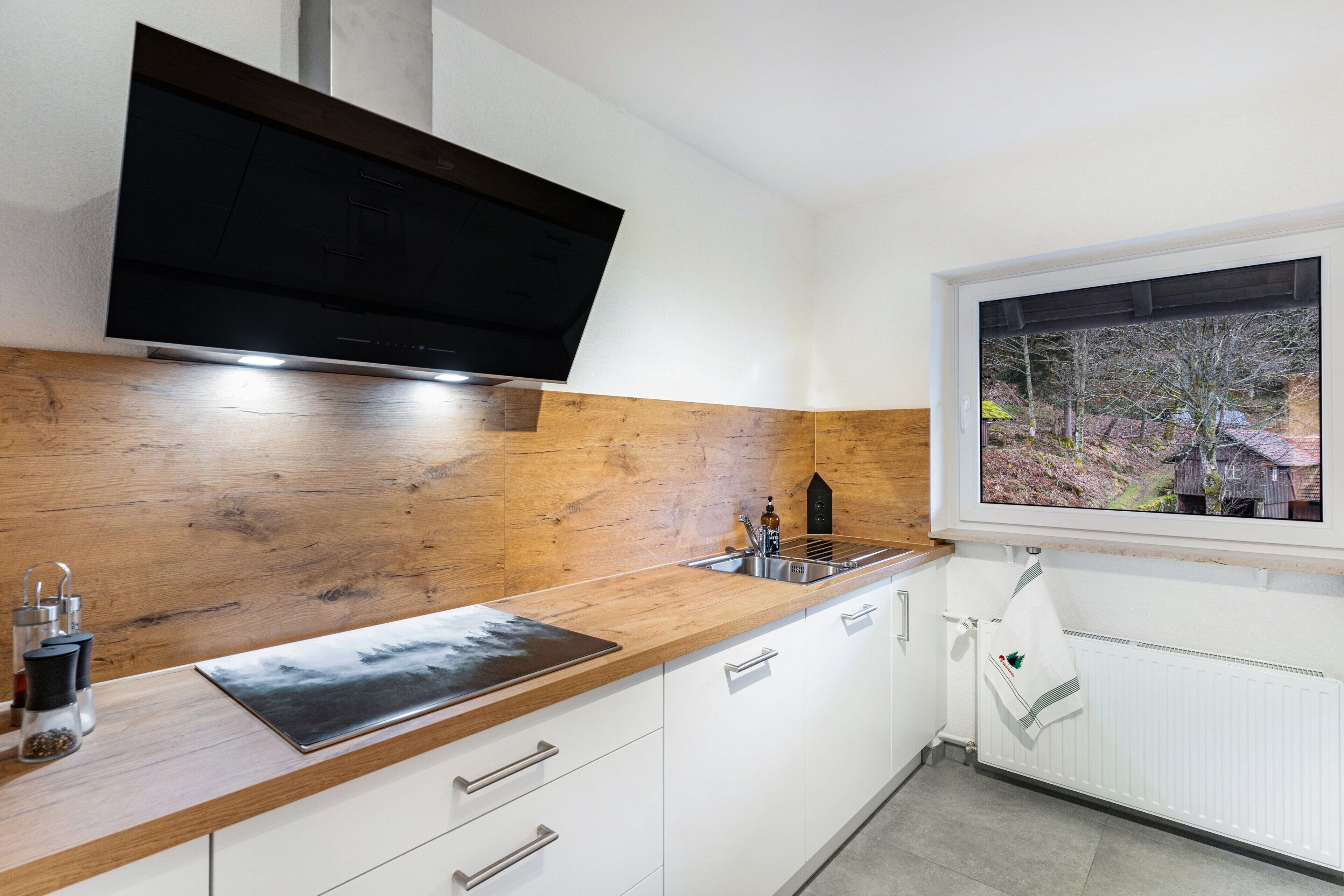 A modern kitchen with a wooden countertop, stainless steel sink, and a large window with a view of trees.