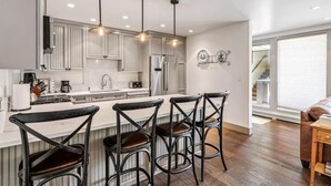 A modern kitchen with white cabinetry, a central island with bar stools, pendant lighting, and a stainless steel refrigerator. - Perfect Location Between Vail & Loinshead (Vail)