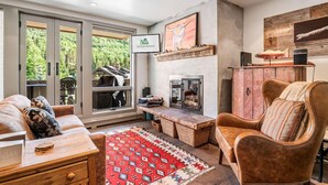 A cozy living room with a fireplace, a comfortable sofa, a wooden coffee table, and a red patterned rug. - Perfect Location Between Vail & Loinshead (Vail)