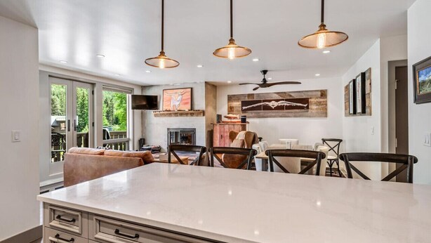 A modern kitchen with a large island, pendant lighting, and a dining area with chairs and a table. - Perfect Location Between Vail & Loinshead (Vail)
