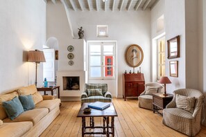 Una sala de estar con sofá, sillón, mesa, chimenea y ventana con marco rojo.