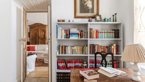 Una habitación con un armario de madera, una estantería llena de libros, una mesa con una lámpara y un cuadro en la pared.