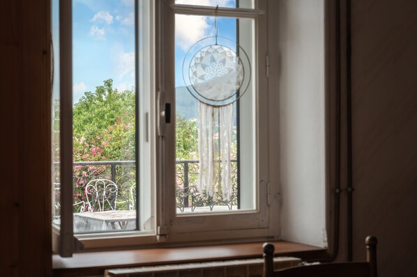 Une fenêtre donnant sur un balcon, un attrape-rêves suspendu et une chaise en métal.