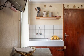 Une cuisine avec un évier blanc, une porte en bois et une étagère contenant des ustensiles de cuisine.
