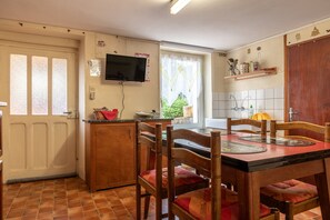Une cuisine avec une table à manger, des chaises, un téléviseur et une fenêtre avec des rideaux.