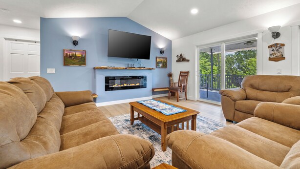 A living room with a fireplace, a flat-screen TV, and a large window. - Accessible Lake and Farm Retreat w/Fresh Eggs, Nature Trails, and Gameroom (Thornfield)