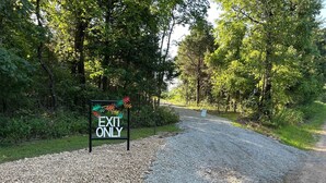 A gravel path leading to an 'EXIT ONLY' sign surrounded by greenery. - Accessible Lake and Farm Retreat w/Fresh Eggs, Nature Trails, and Gameroom (Thornfield)