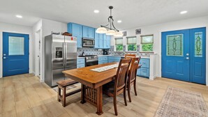 A modern kitchen with blue cabinets, stainless steel appliances, and a wooden dining table. - Accessible Lake and Farm Retreat w/Fresh Eggs, Nature Trails, and Gameroom (Thornfield)