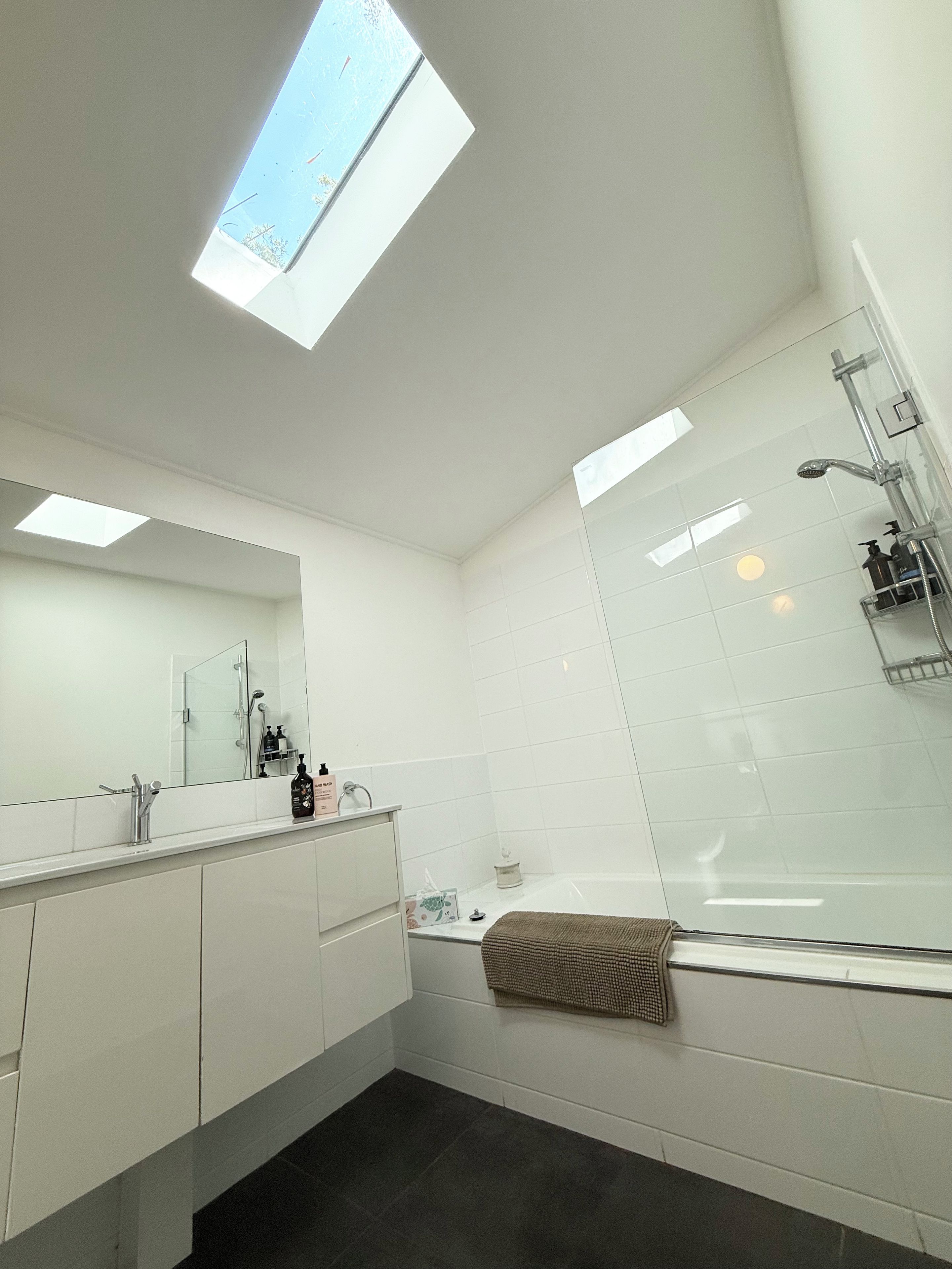Un baño moderno con tragaluz, ducha con cerramiento de vidrio y un espejo grande.