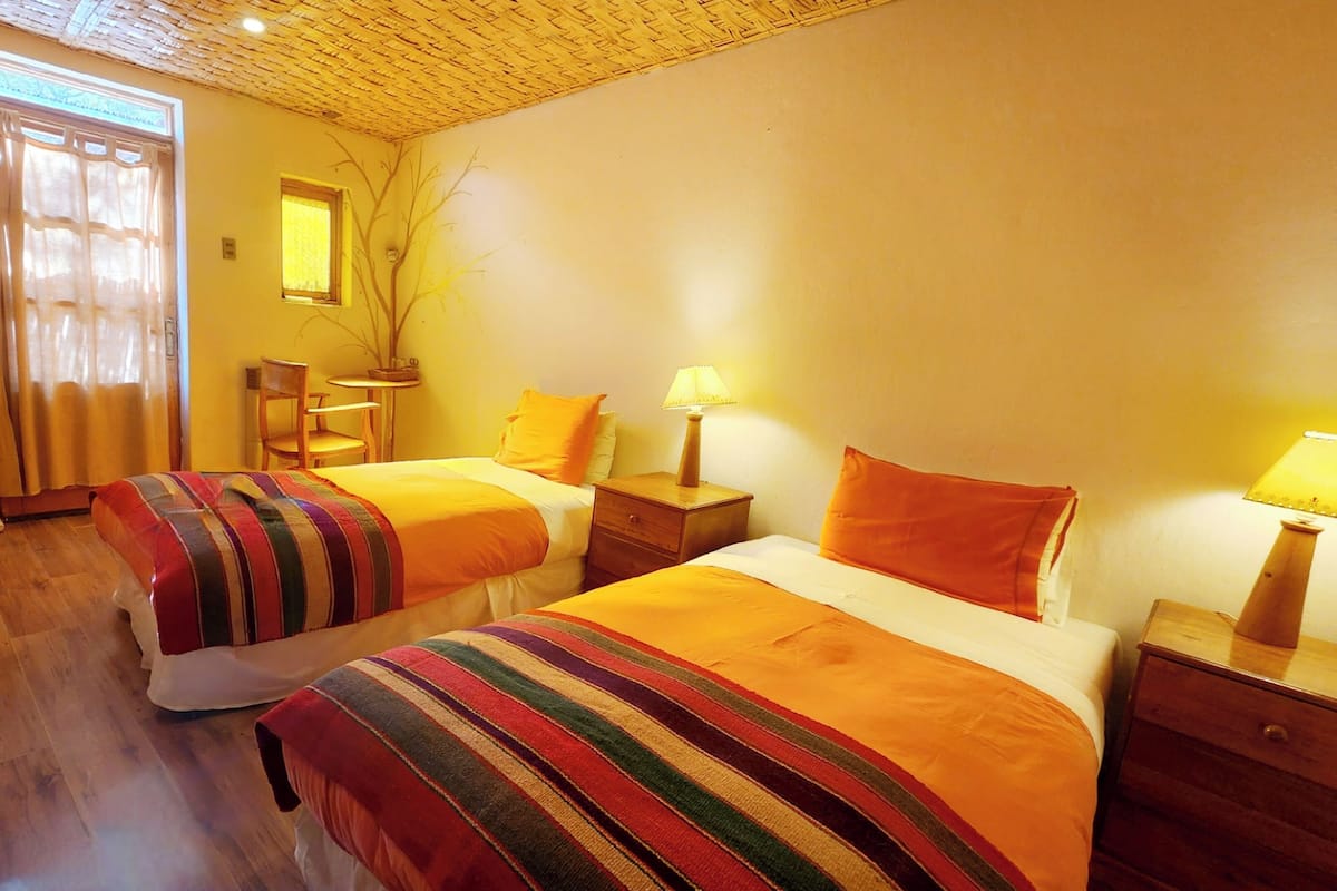 Habitació d'hotel amb dos llits, una taula petita, una cadira i una làmpada.