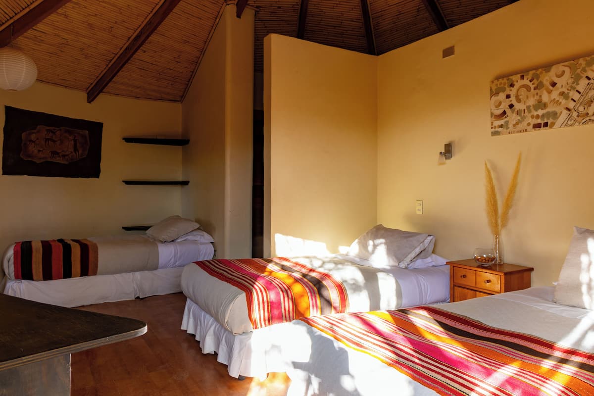 Una habitació amb dos llits, una taula de fusta i una nitze amb un ram.