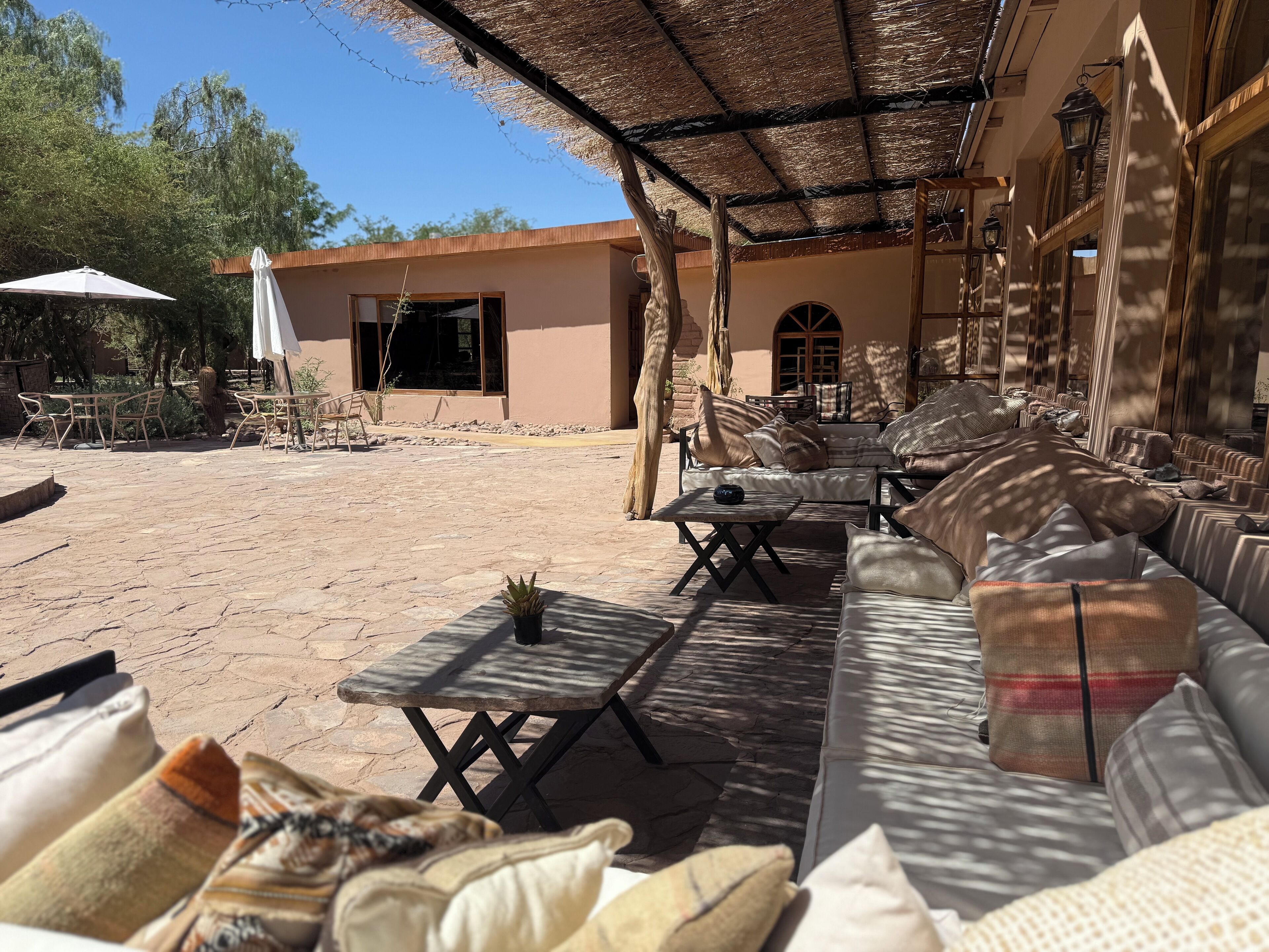 An outdoor seating area with a thatched roof, stone flooring, and a mix of sofas and tables.