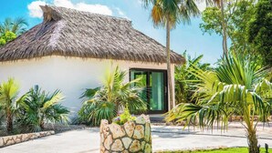 A thatched-roof building with a stone planter and tropical plants.