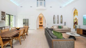 A spacious living area with a dining table, sofa, and a high ceiling with skylights.