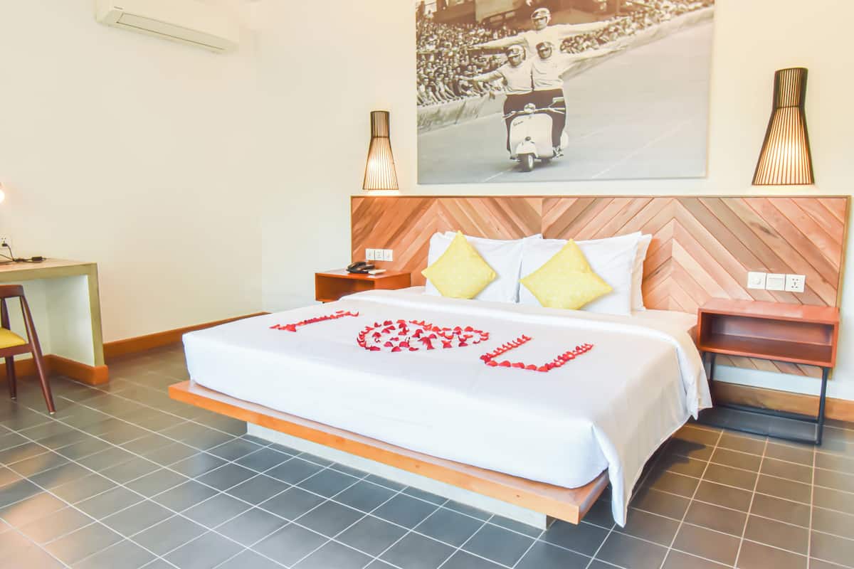 A hotel room with a bed, a nightstand, a desk, and a wall-mounted lamp.