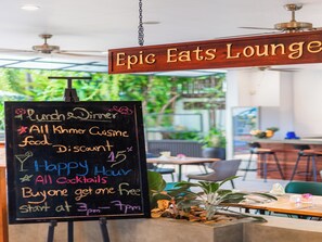A chalkboard menu at Epic Eats Lounge advertising lunch and dinner, all Khmer cuisine, a 15% discount, happy hour, all cocktails, and a buy-one-get-one-free offer starting at 3pm.