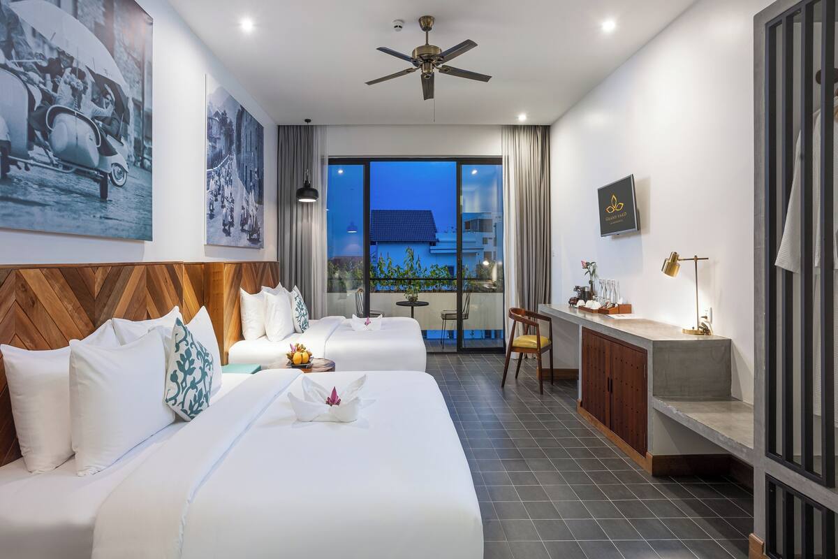 A hotel room with two beds, a desk, a chair, a ceiling fan, and a balcony with a view.