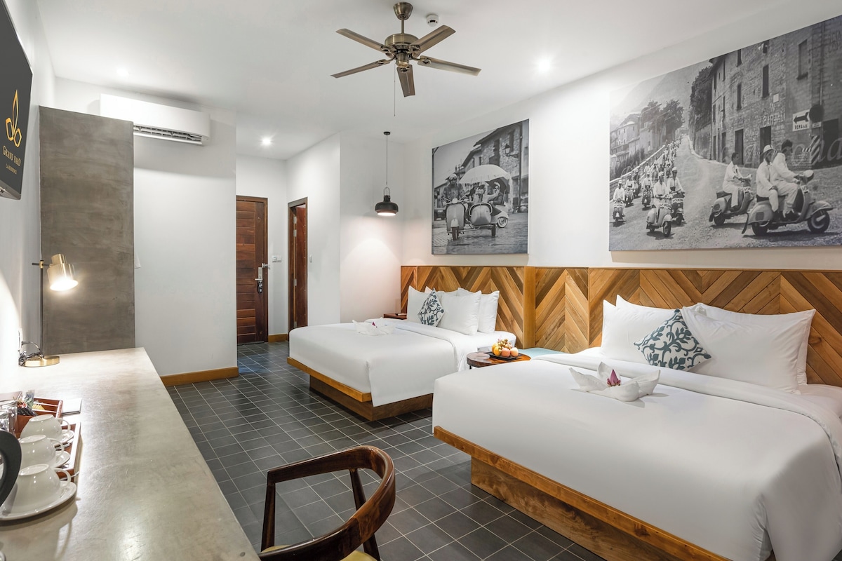 Quarto de hotel com duas camas, uma escrivaninha, uma cadeira e uma mesa de jantar.