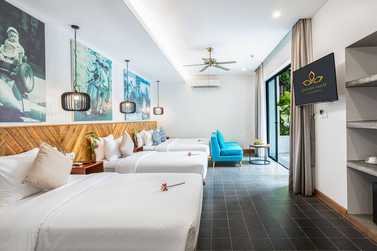 A hotel room with two beds, a blue chair, a TV, and a ceiling fan.