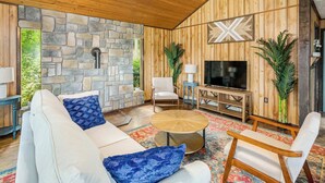Un salon chaleureux avec un mur en pierre, un lambris en bois, un téléviseur et des sièges confortables.