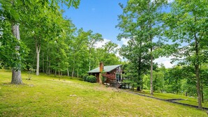 Une cabane rustique avec une cheminée, entourée d’une végétation luxuriante et bordée d’une petite voie ferrée.