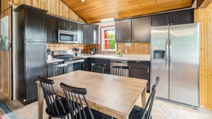 Une cuisine moderne avec des meubles de couleur sombre, des appareils électroménagers en acier inoxydable et une table à manger en bois.