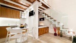 Eine moderne Küche mit weißen Stühlen, einem Esstisch und einer Holztreppe mit Glastrennwand.