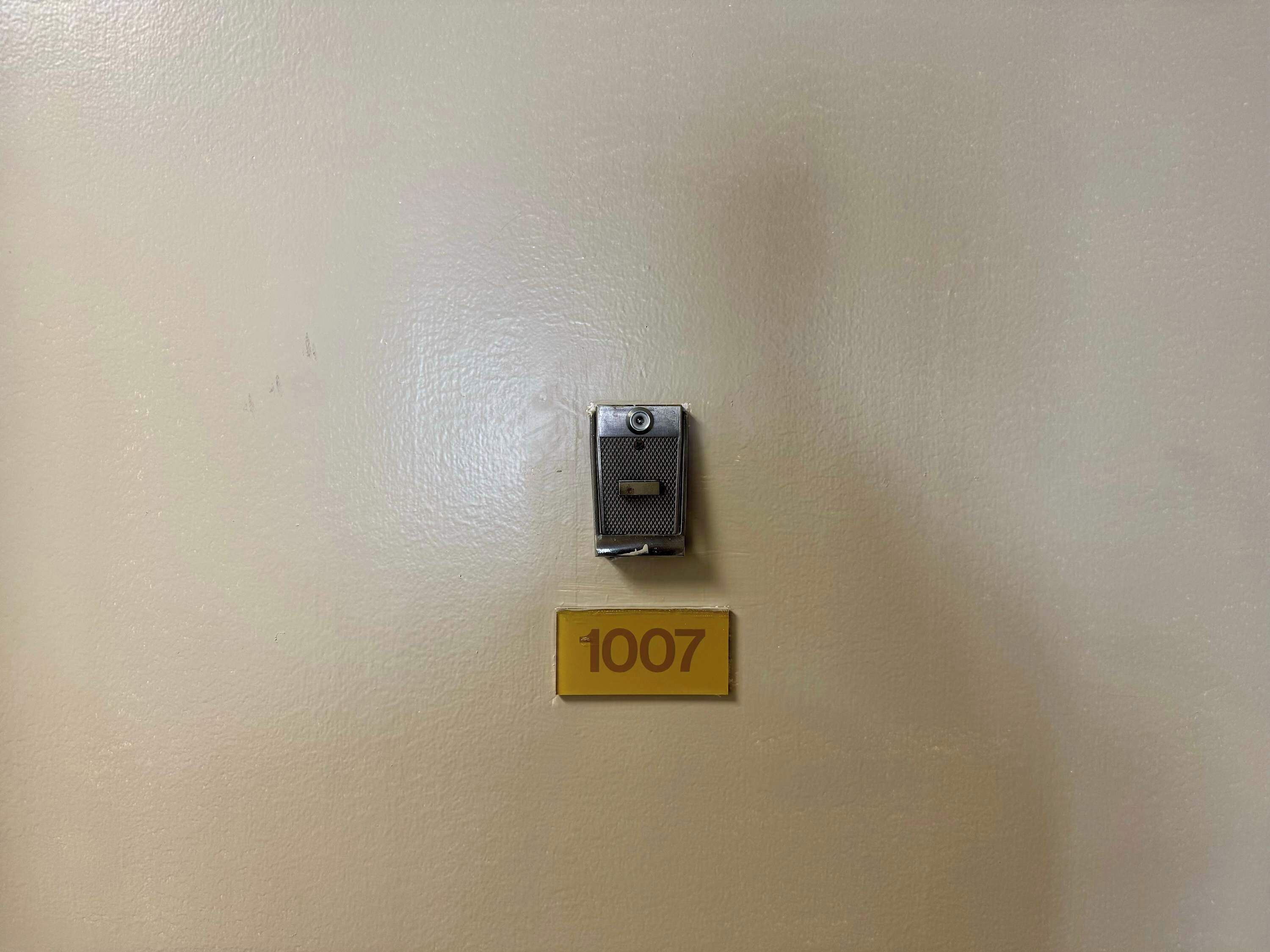 Un interphone fixé au mur et une plaque indiquant le numéro de la chambre, de couleur jaune.