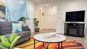 A modern living room with a grey sofa, a colorful rug, a marble coffee table, and a TV on a black cabinet. - Historic Condo in Atlanta with Skyline View (Atlanta)
