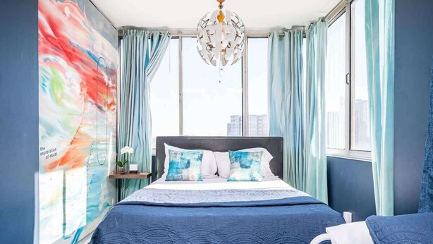 A bedroom with a bed, a nightstand, a window with curtains, and a wall with a colorful abstract painting. - Historic 1B/1B Condo in Atlanta (Atlanta)