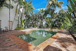A swimming pool with a curved edge, surrounded by palm trees and a paved walkway.