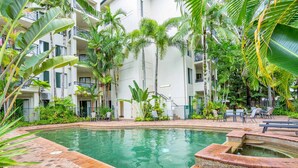 Una piscina rodeada de exuberante vegetación y un edificio de varios pisos con balcones.