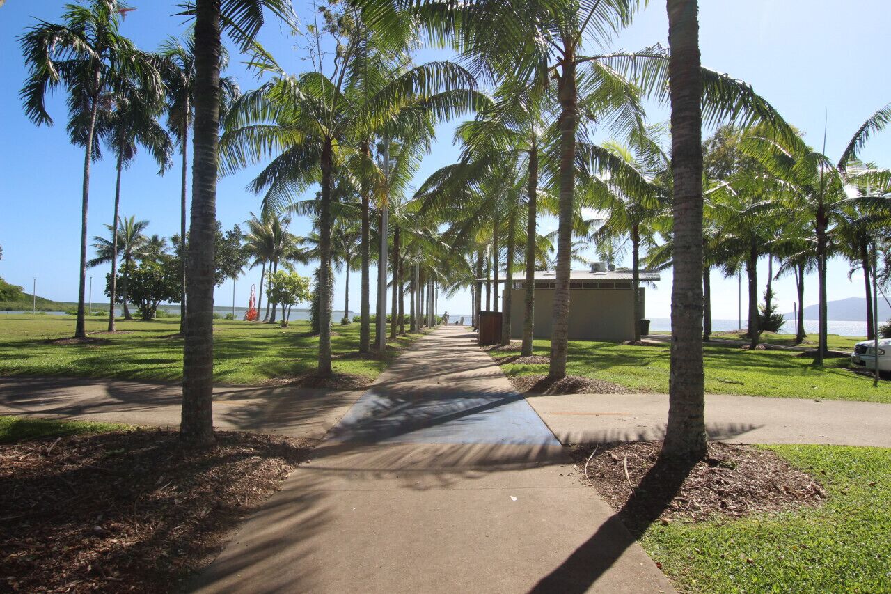 A pathway lined with palm trees leading to a building with a view of the ocean.