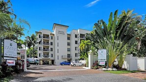 Un edificio de hotel de varios pisos con un letrero que indica 'TROPIC TOWERS' y espacio de estacionamiento para visitantes.