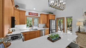 A modern kitchen with wooden cabinets, a stainless steel refrigerator, and a large island with a plant centerpiece.