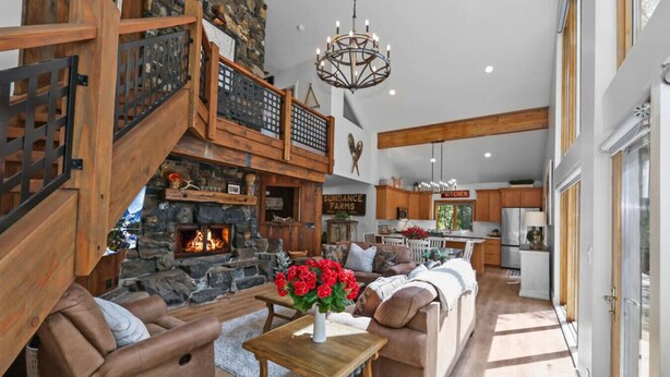 A spacious living area with a stone fireplace, wooden staircase, and a modern kitchen in the background.