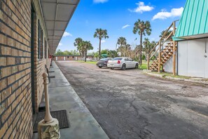 A parking area with a brick building, a covered walkway, and two cars parked. - Mathis Motel (Mathis)
