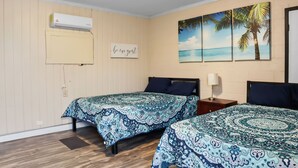 A room with two beds, an air conditioner, a 'be our guest' sign, and a beach-themed wall art. - Mathis Motel (Mathis)