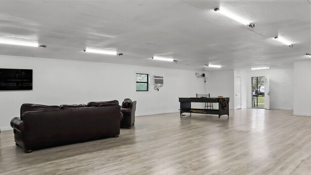 A spacious room with a wooden floor, a brown sofa, a black table, and a door leading outside. - Mathis Motel (Mathis)