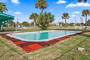 A swimming pool with a red and white border, surrounded by grass and palm trees. - Mathis Motel (Mathis)