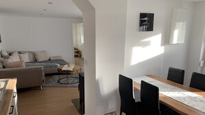 A modern living room with a sofa, a dining table with chairs, and a kitchen area. - NEW renovated vacation apartment in a quiet location (large fenced property) (Plau am See)