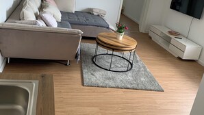 A modern living room with a sofa, a coffee table, a TV, and a white cabinet. - NEW renovated vacation apartment in a quiet location (large fenced property) (Plau am See)