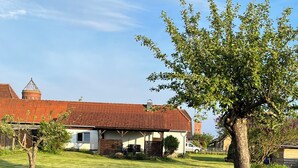 A grassy area with a building featuring a red-tiled roof and a small tree. - NEW renovated vacation apartment in a quiet location (large fenced property) (Plau am See)