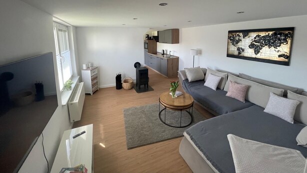 A modern living room with a sofa, coffee table, and a kitchen area in the background. - NEW renovated vacation apartment in a quiet location (large fenced property) (Plau am See)