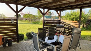 An outdoor patio with a table and chairs, a grill, and a covered area with a wooden roof. - NEW renovated vacation apartment in a quiet location (large fenced property) (Plau am See)