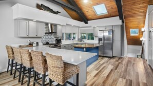 A modern kitchen with a large island, bar stools, stainless steel appliances, and a wooden ceiling. - Outstanding Ocean Front Home, Pet Friendly, Hot Tub, Pool Table, Games, Seconds From Beach (Rockaway Beach)