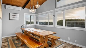 A dining area with a wooden table and benches, large windows with a view of the outdoors, and a ceiling with exposed beams. - Outstanding Ocean Front Home, Pet Friendly, Hot Tub, Pool Table, Games, Seconds From Beach (Rockaway Beach)