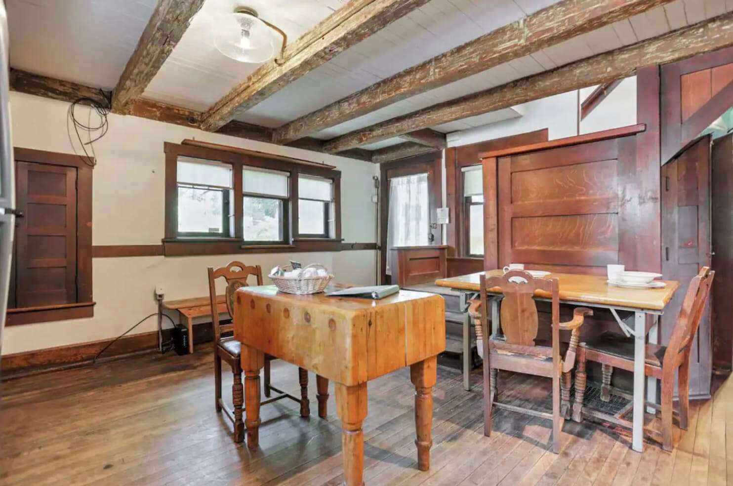 A rustic dining room with wooden furniture, exposed beams, and large windows.