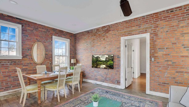 Comedor con pared de ladrillo, televisor y mesa con sillas.