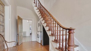 Una escalera de madera con barandilla, que lleva a una habitación con una puerta blanca y un banco.